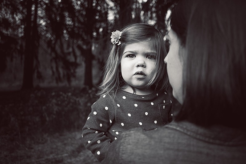 A black and white images with toddler girl looking over her mother's shoulder
