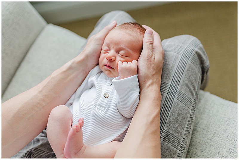 Newborn baby boy in white onesie laying in dad's lap