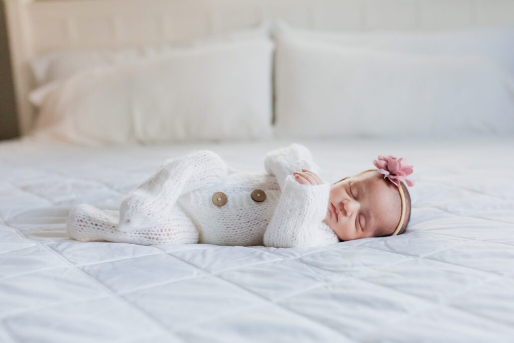 Newborn baby girl laying sleeping on a white bedspread